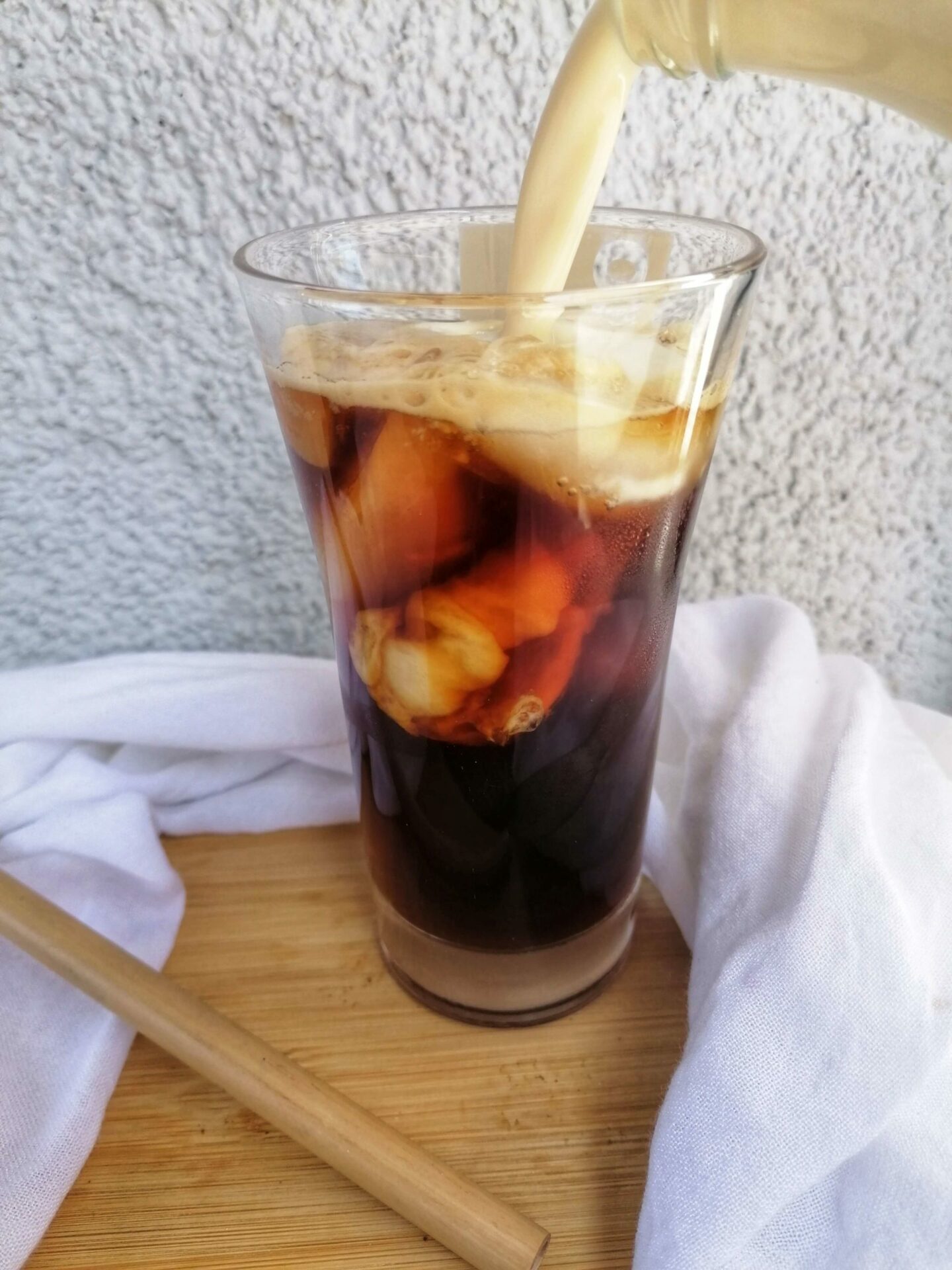 Das Bild zeigt einen Iced Coffee einfach selbstgemacht in der Entstehung. In ein Glas mit Eiswürfeln und Kaffee wird Milch gegossen