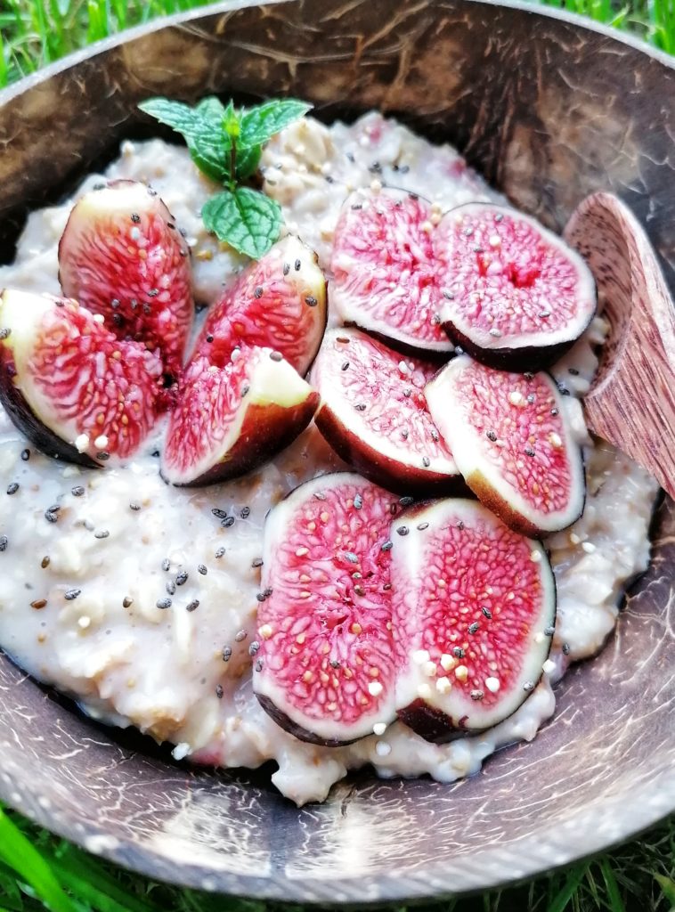 Das Bild zeigt ein angerichtetes Porridge in der Kokosnuss Schale. Garniert mit aufgeschnittenen Feigen und einem grünen Minzblatt.